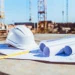Building plans and a hard hat are shown with construction in the background.
