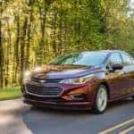 A red 2015 Chevy Cruze is driving on a sunny road in Dayton, OH.