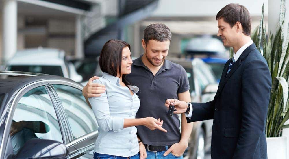 A salesman is handing a couple keys to their new, used car in Dayton, OH.