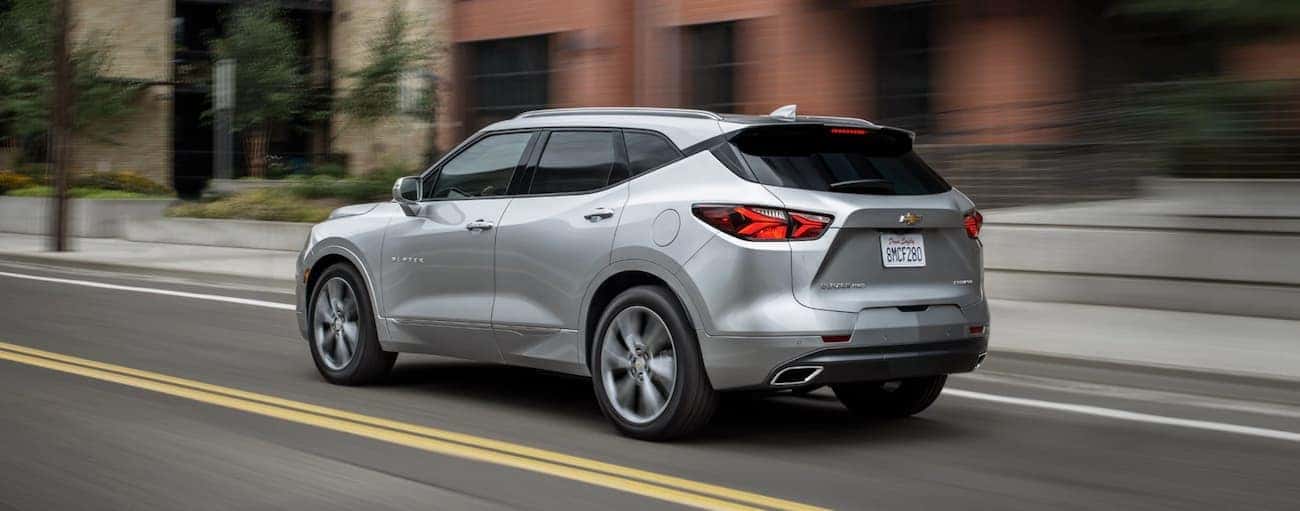 A silver 2019 Chevy Blazer is driving past brick buildings.