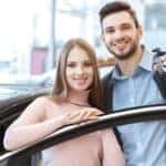 A smiling couple is holding car keys up to their new car that they bought at a Buy Here Pay Here in Indianapolis, IN.