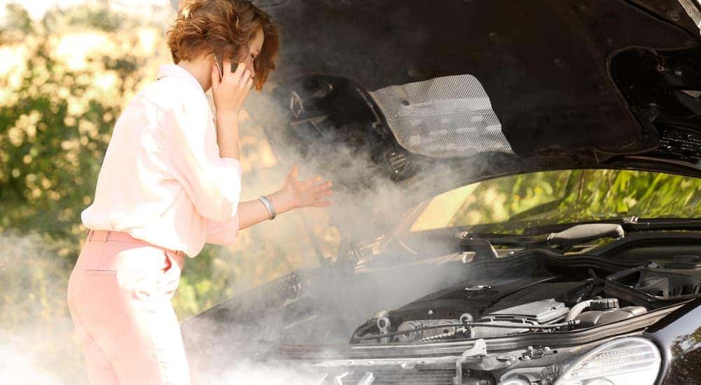 A woman is on the phone while on the side of the road near Cincinnati, OH, with smoke coming out of her car.
