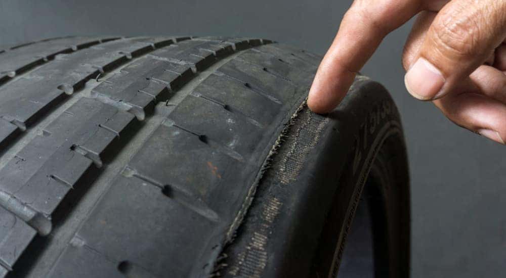A finger is pointing to wear on a tire, which is a common clue that you need new tires in Cincinnati, OH.