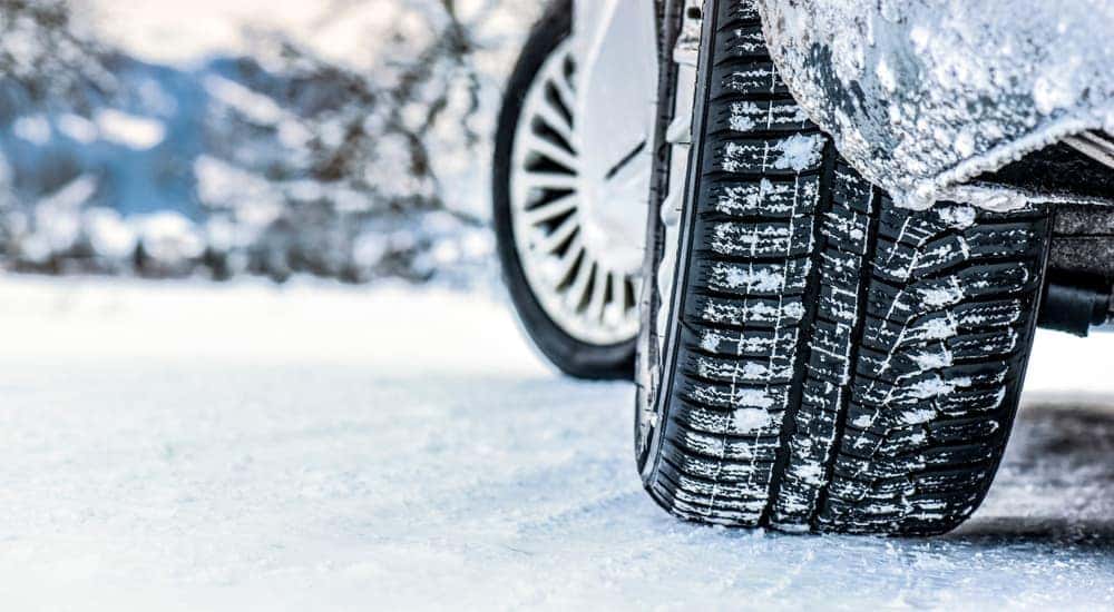 A close up of a car with winter tires driving on snow in Cincinnati, OH is shown.