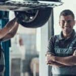 A smiling mechanic is at a local garage working on one of many great used cars in Columbus, Ohio.