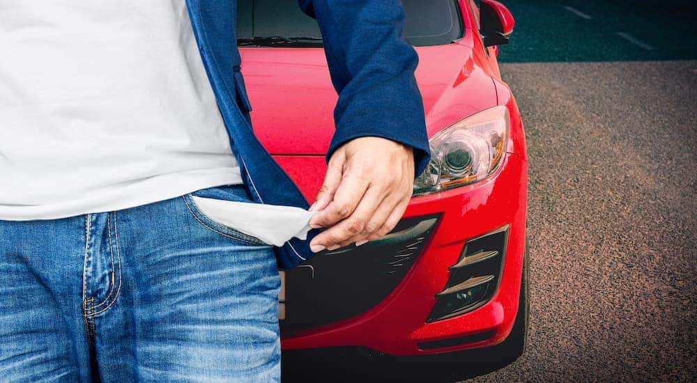 A closeup shows a turned out pocked of a man with bad credit in front of a red car.