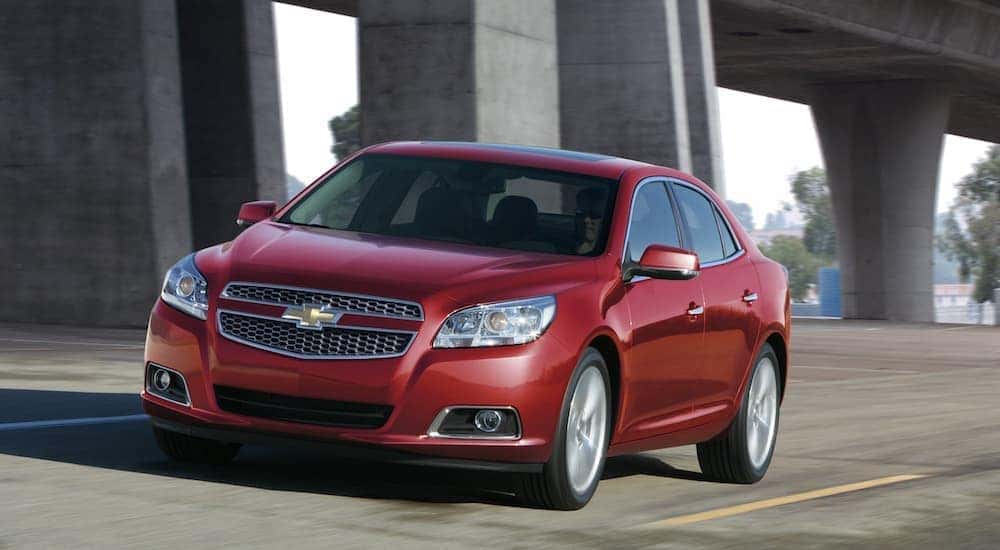 A red 2013 Chevy Malibu, which is a popular option among used cars, is driving under a Cincinnati, OH, bridge.