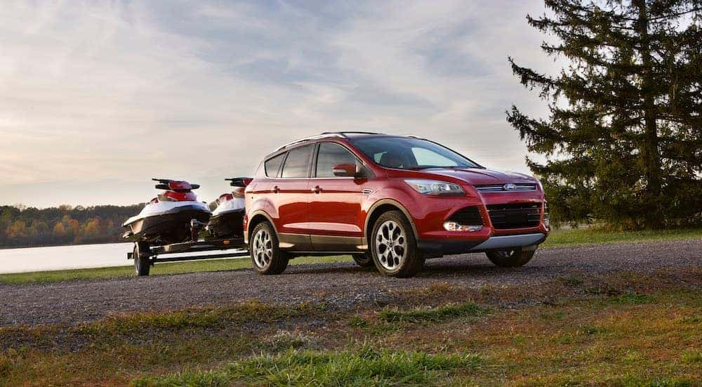 A red 2014 Ford Escape is parked in front of a lake with jetskis on a trailer.