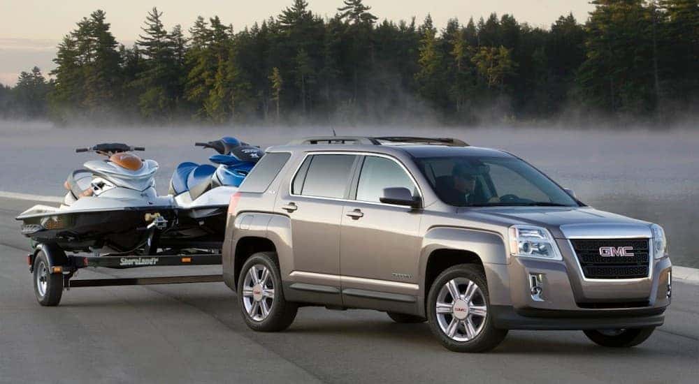 A grey 2015 GMC Terrain is parked in front of a misty pond with jetskis on a trailer.