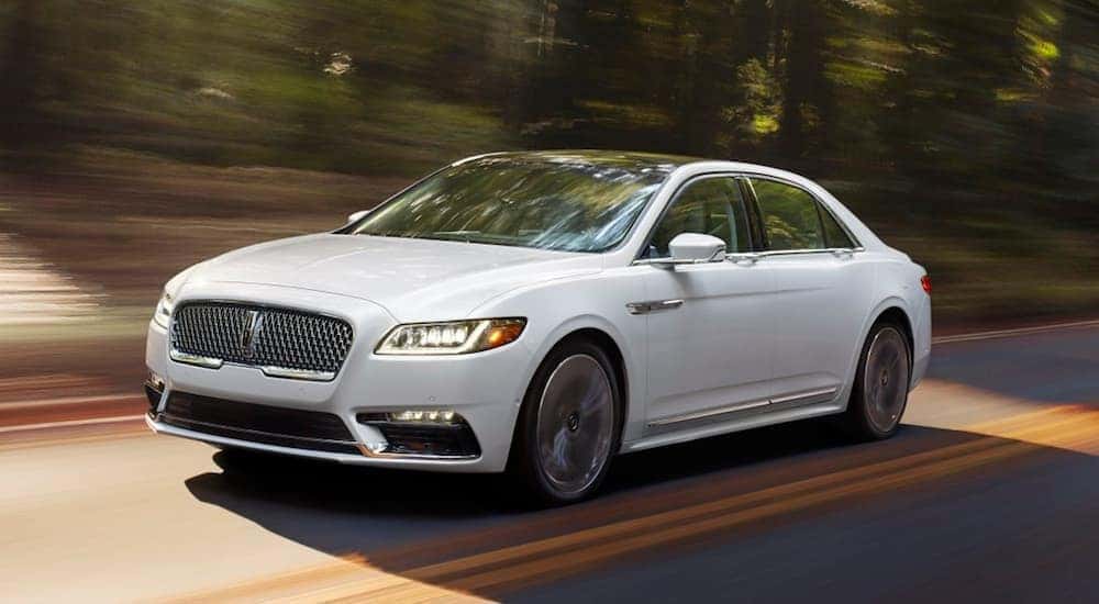A white 2017 Lincoln Continental, which is a popular option among luxury used cars, is driving on a tree lined road.