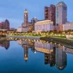 The Columbus, OH city skyline is shown at dusk.