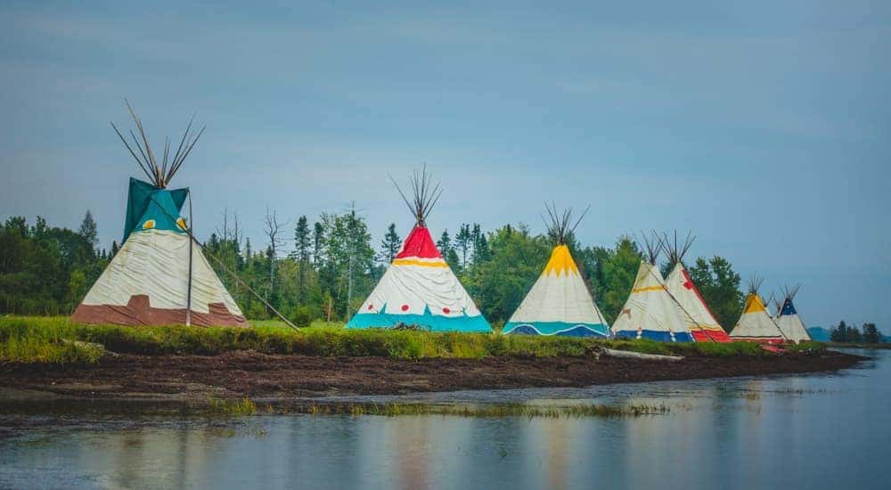 A row of teepees are shown next a river.