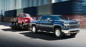 A dark blue 2020 Chevy Silverado 2500HD is towing an antique Chevy truck.