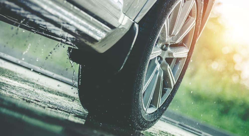 A close up of a tire on a silver car in the rain is shown.