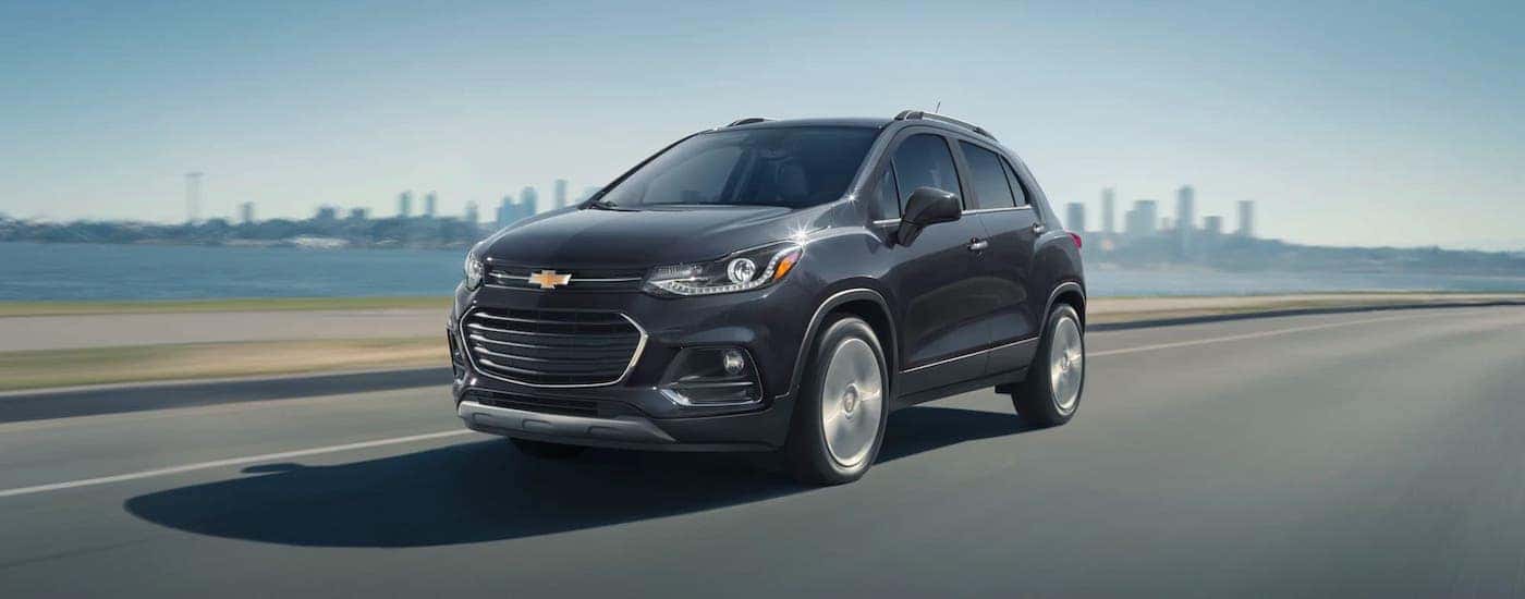 A dark blue 2020 Chevy Trax is driving on a highway away from a city.