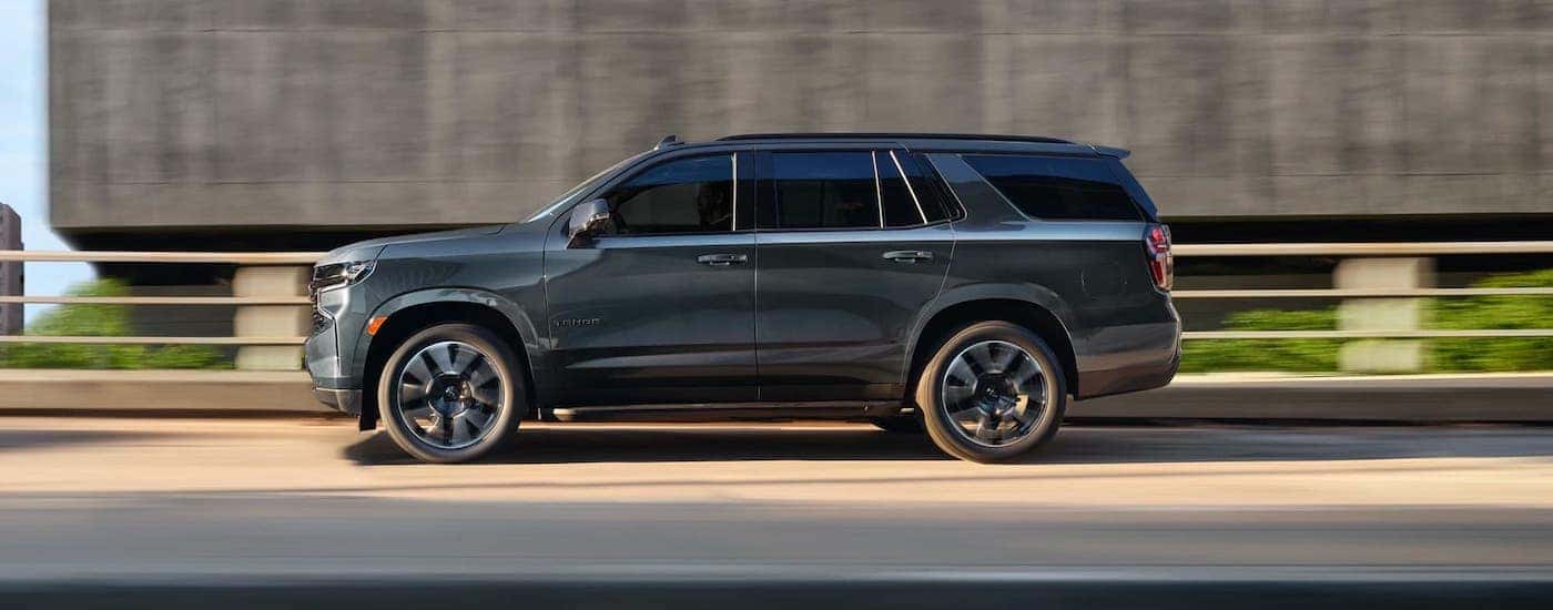 A gray 2021 Tahoe is driving on a highway and shown from the side, this is a great SUV in the 2021 Chevy Tahoe vs 2020 Chevy Tahoe comparison.