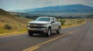 A silver 2020 Chevy Silverado without Silverado mud flaps is driving on a highway.