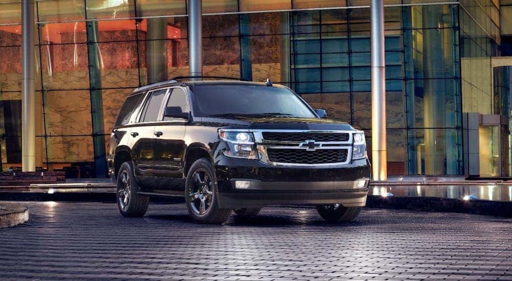 A popular used car in Cincinnati, a black 2017 Chevy Tahoe, is parked in front of glass building.