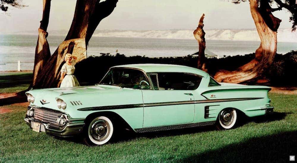 A teal 1958 Chevy BelAir Impala is parked in front of a beach.