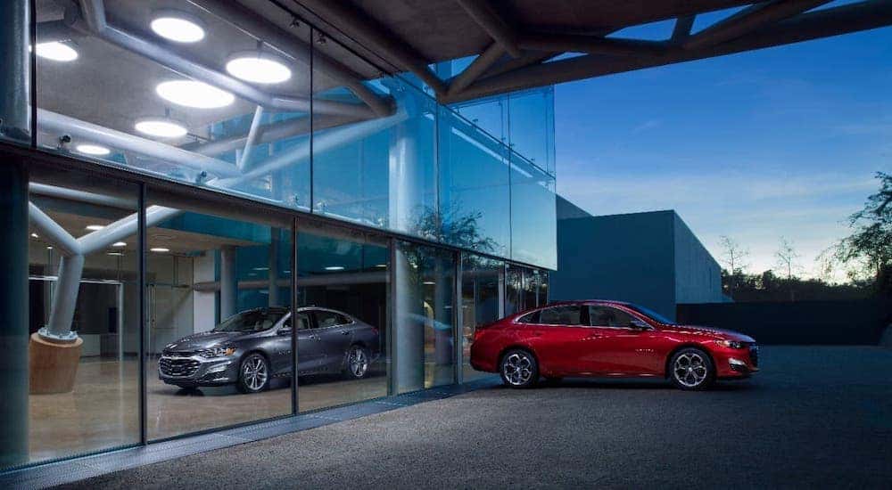 A red and a silver 2019 Chevy Malibu are parked at a used car dealership in Cincinnati, OH.
