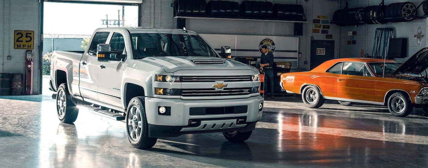 A white 2017 Chevy Silverado 2500 HD LTZ is shown in a garage parked next to an orange muscle car.
