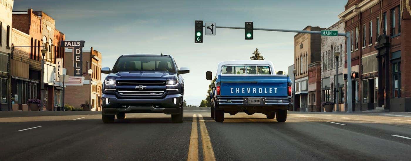 A dark blue 2018 Chevy Silverado 1500 Z71 Centennial Edition is driving past a light blue 1972 C10 at a set of traffic lights.