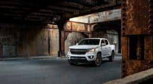 One of the most popular used Chevy Trucks, a white 2019 Chevy Colorado RST, is shown parked under a rusty bridge.