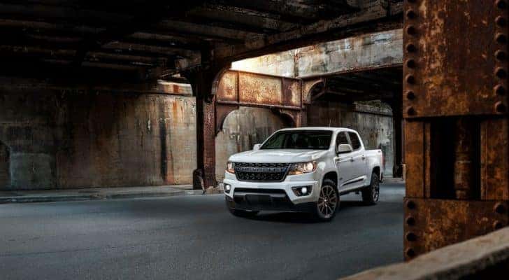 One of the most popular used Chevy Trucks, a white 2019 Chevy Colorado RST, is shown parked under a rusty bridge.