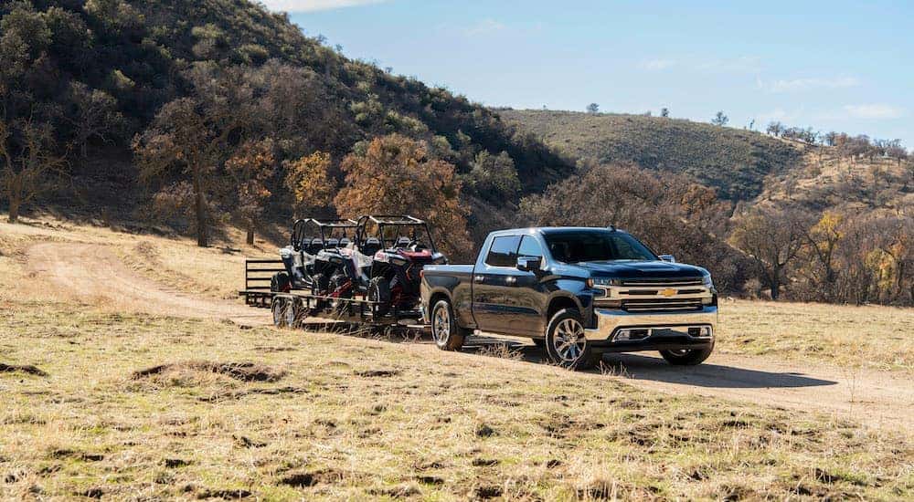 A popular Chevy truck, a black 2020 Chevy Silverado Duramax, is towing a trailer with two UTVs.