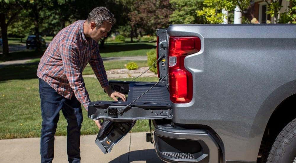 A man is opening the Multi-Flex tailgate on a grey 2021 Chevy Silverado.