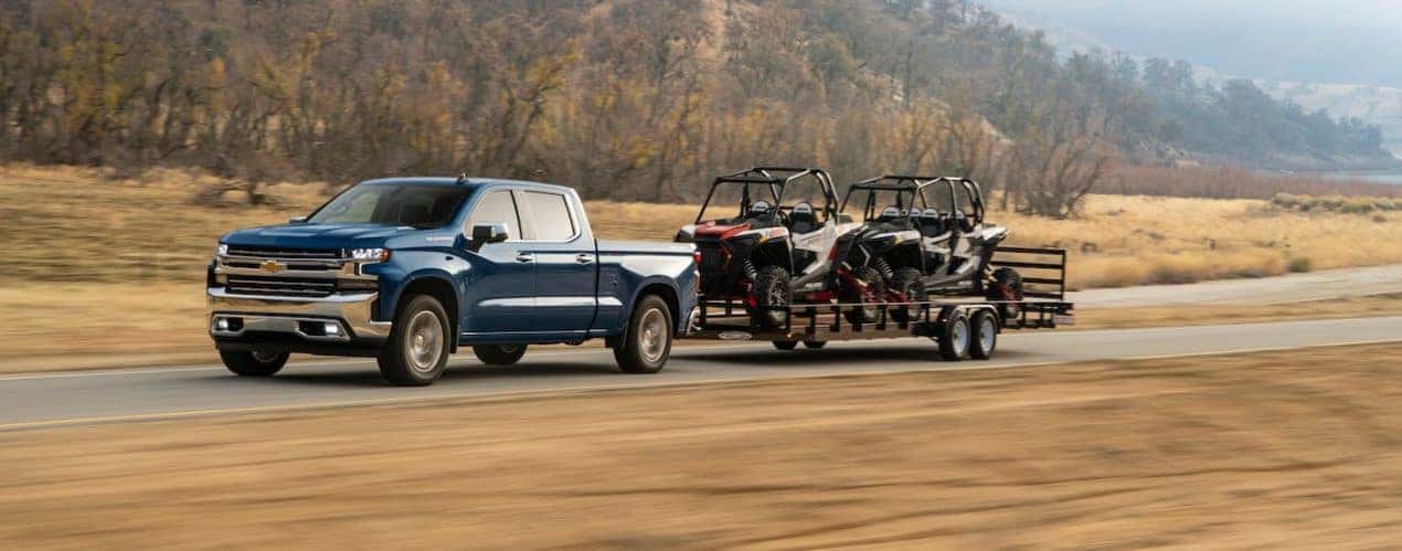 A blue 2021 Chevy Silverado 1500 diesel is towing a trailer with 2 side-by-sides.