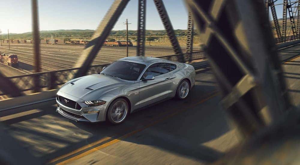 A silver 2020 Ford Mustang is shown from a high angle, driving over a bridge and train yard.