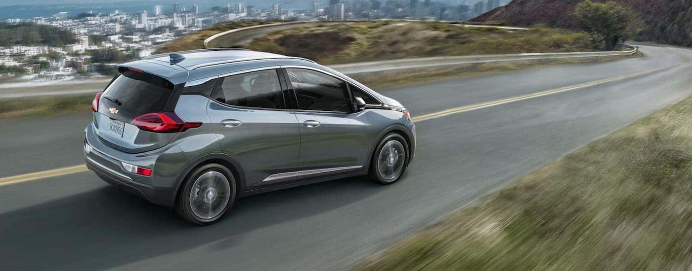 A silver 2021 Chevy Bolt EV is driving on a winding road to a city below.