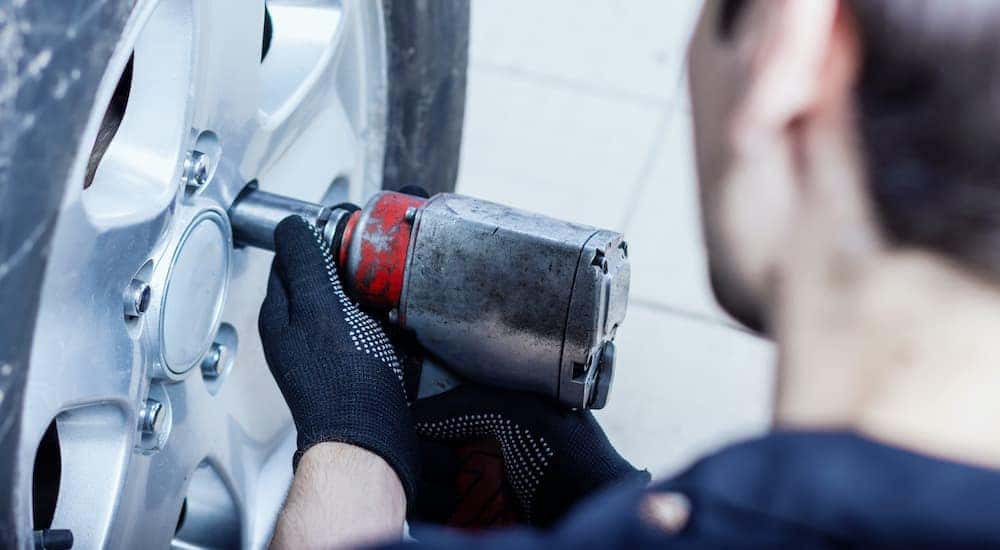 In Cincinnati car tires are being installed on a vehicle by a mechanic with an impact gun.