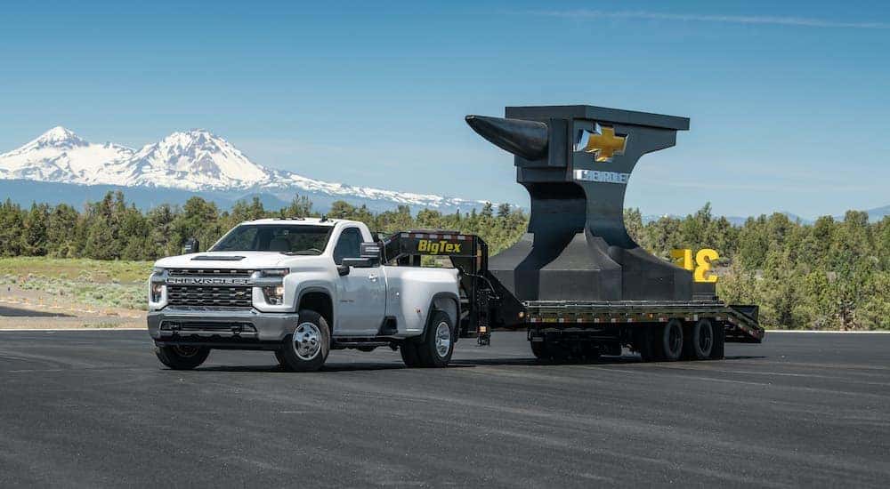 A white 2020 Chevy Silverado 3500HD is towing a gooseneck trailer with a large anvil brandishing the Chevy bowtie logo.
