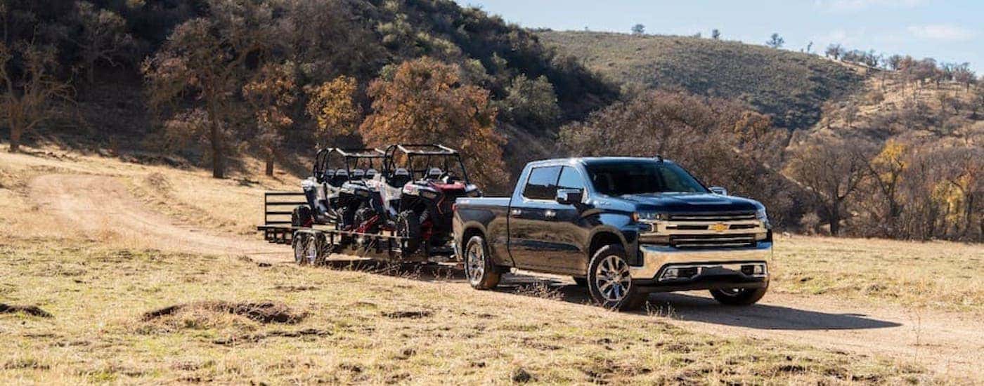 A popular used diesel truck, a black 2020 Chevy Silverado 1500 is shown towing a trailer loaded with dirt bikes.