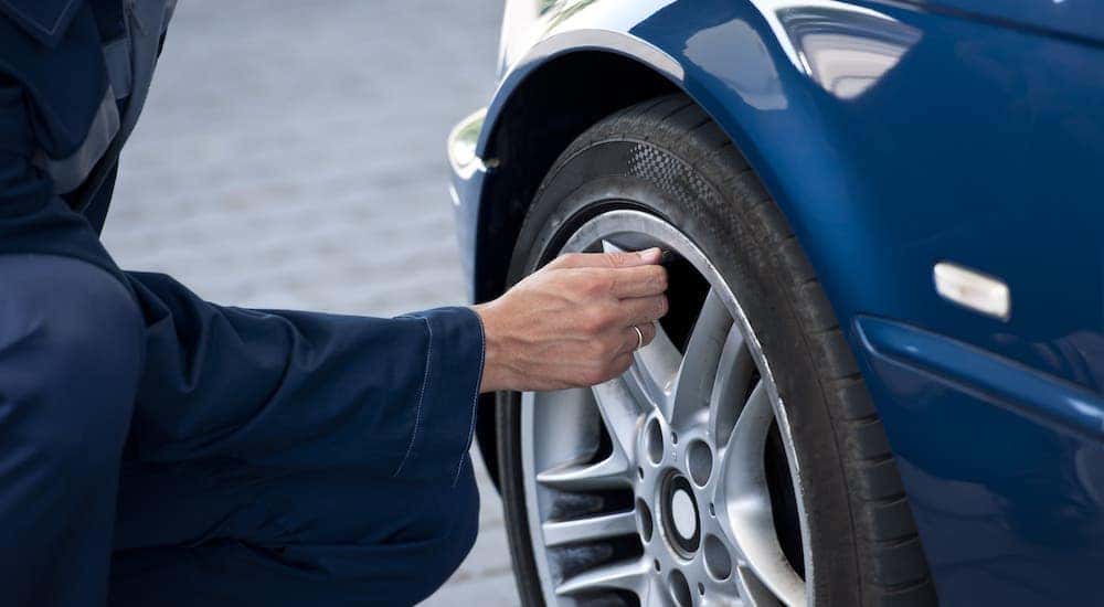 A mechanic is tightening the valve cover on the tire of a blue car.