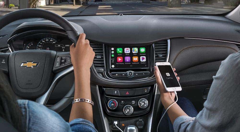 A passenger is using a phone and Apple CarPlay in a 2020 Chevy Trax while someone else drives.