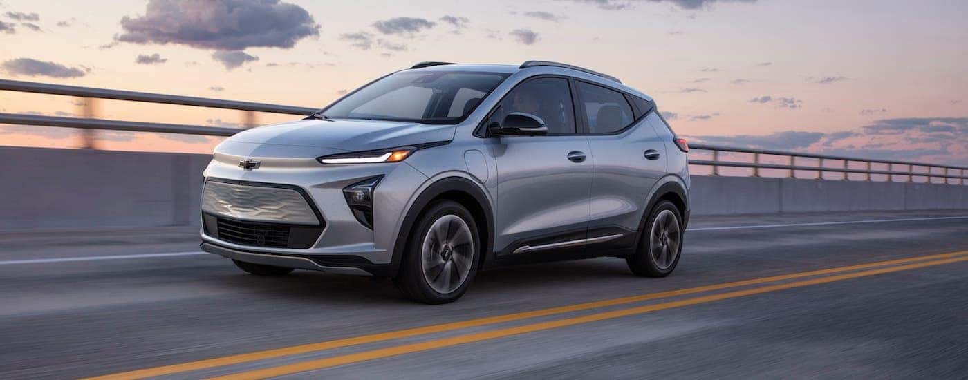 A silver 2022 Chevy Bolt EUV is driving on a highway at dusk.