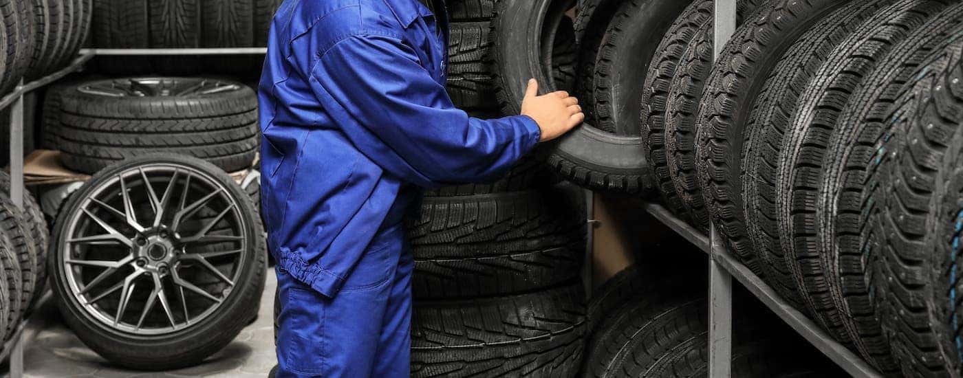 A mechanic in a blue jumpsuit is taking a tire off of a rack.