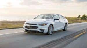 A white 2018 Chevy Malibu is driving on a coastal highway.