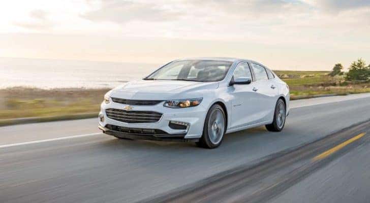 A white 2018 Chevy Malibu is driving on a coastal highway.