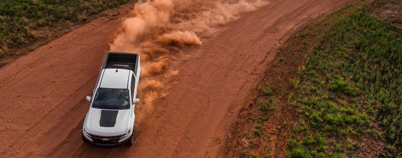A silver 2017 Chevy Colorado ZR2 is is shown from a high angle, driving on a dirt path kicking up sand.