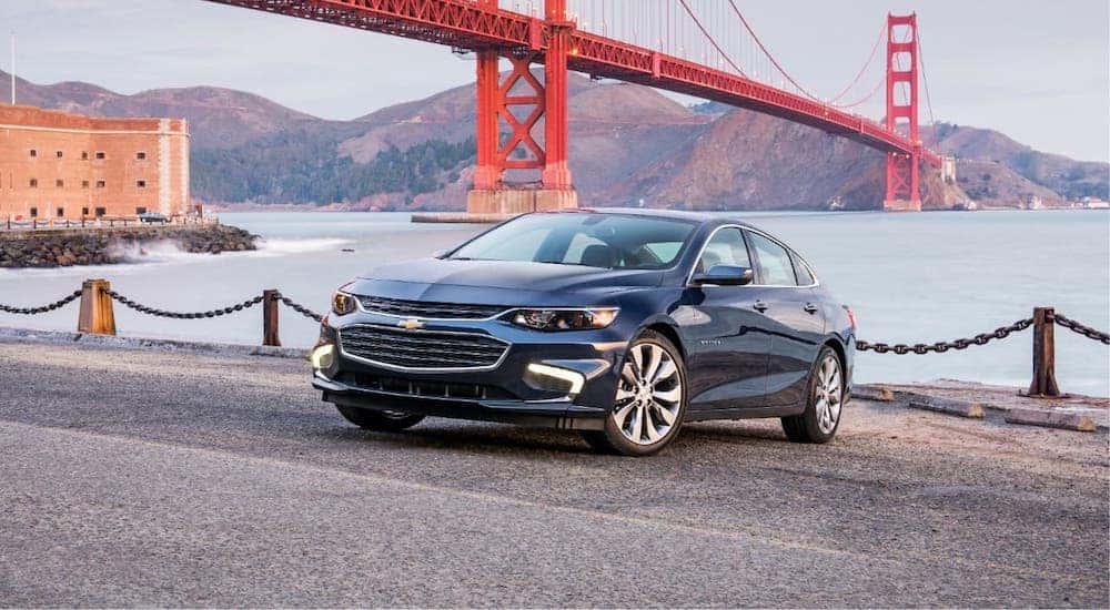 A dark blue 2018 Chevy Malibu is parked in front of the golden gate bridge.