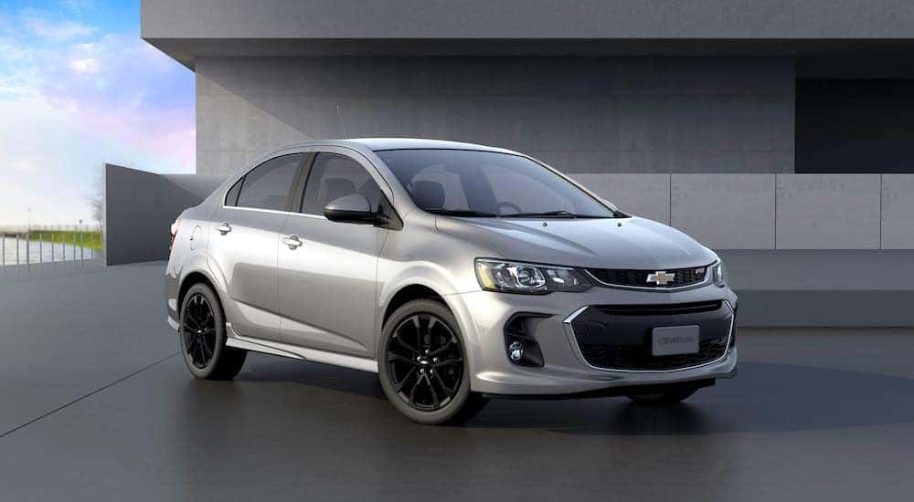 A silver 2020 Chevy Sonic is parked in front of a modern building.