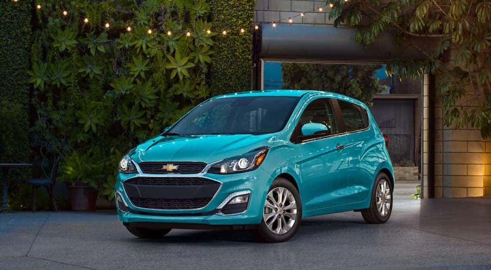 A teal 2021 Chevy Spark is parked under string lights, in front of foliage.