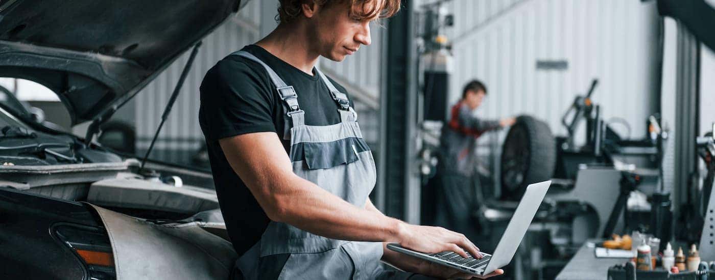 A close up shows a mechanic using a laptop in a repair shop.
