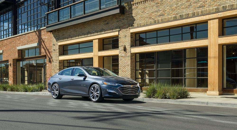A gray 2020 Chevy Malibu is parked near a modern building after leaving a used car dealer near you.