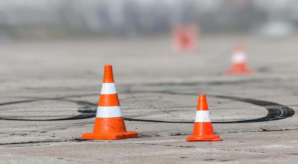 A close up shows orange and white cones in an empty lot with tire marks on the pavement.