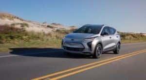A silver 2022 Chevy Bolt EUV is driving in front of a sandy hill.
